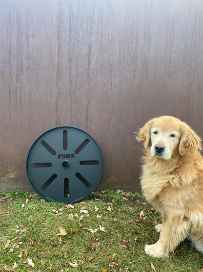 A large metal strongman wagon wheel from FORS displayed outdoors beside a golden retriever, showcasing strongman equipment for training and CrossFit use.